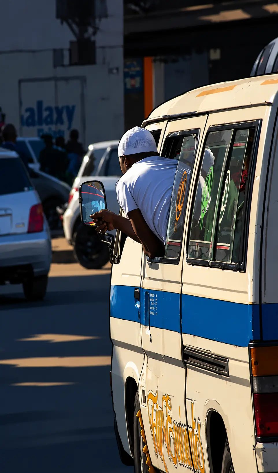Photo-illustration : un apprenti penché à la portière d’un minibus de transport, dans la circulation
